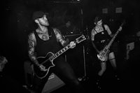 a black and white photo of two people playing guitars in a dark room